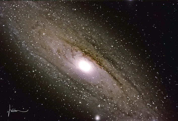 The Andromeda Galaxy, a bright elliptical core with dust lanes, against a dense star field.