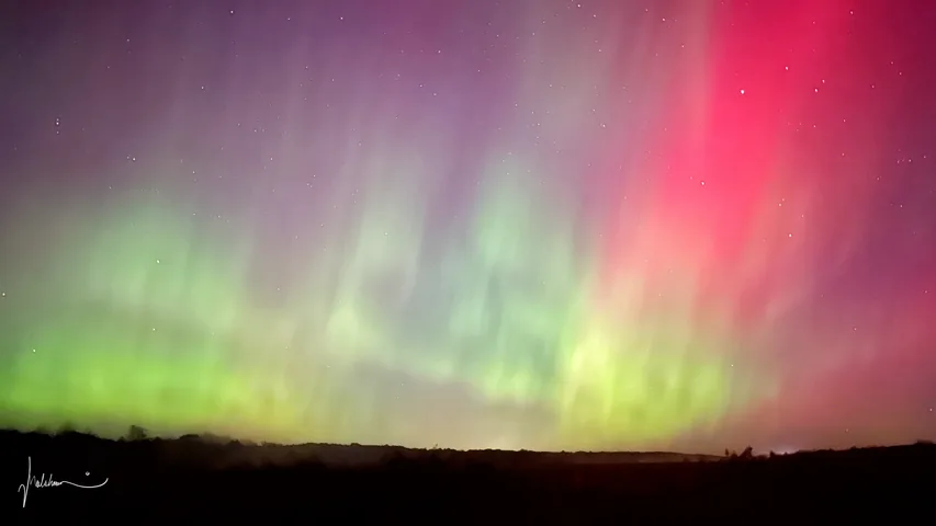 Green and vivid red aurora curtains filling the sky above a dark horizon.
