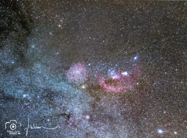A wide field of the Orion region with faint red arcs of Barnard's Loop and pink nebulae.