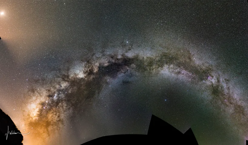 The Milky Way arching across the whole sky above dark silhouetted hills.